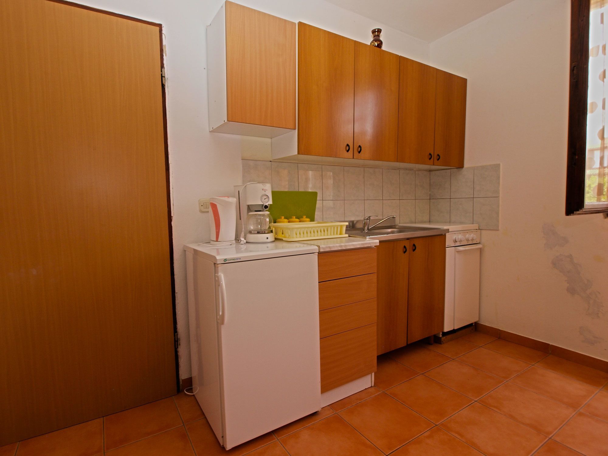 A compact kitchen with wooden cabinets, a white refrigerator, a coffee maker, and a sink.