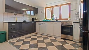 A modern kitchen with dark cabinets, a checkered floor, and stainless steel appliances. - Apartment Marija 85 (Fazana)