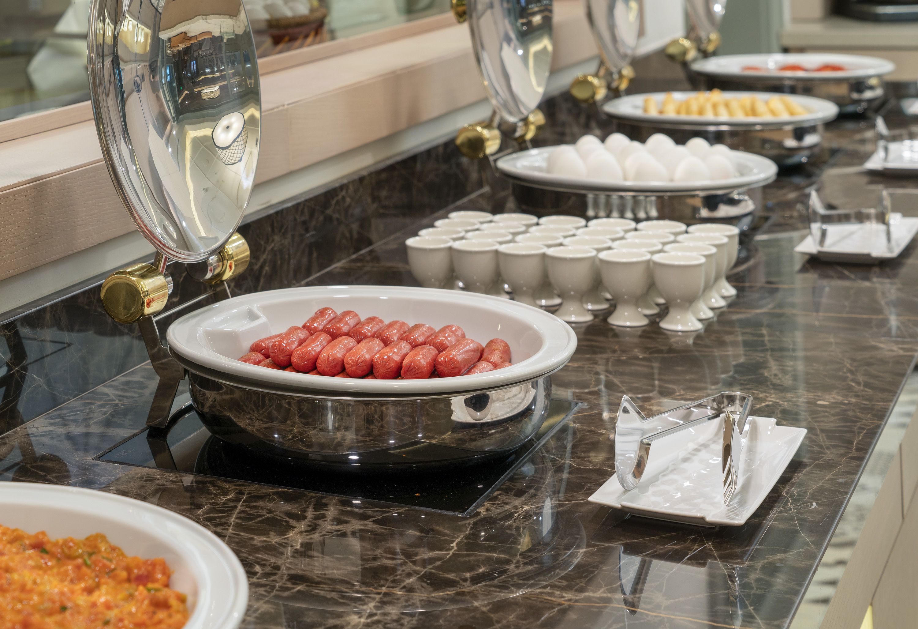 A buffet setup with various dishes including sausages, eggs, and other food items.