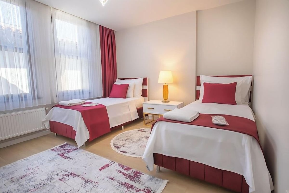 Hotellihuone, jossa on kaksi sänkyä, yöpöytä, lamppu ja ikkuna, jossa on verhot.
