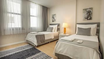 A hotel room with two beds, a large window with sheer curtains, a patterned rug, and artwork on the walls.