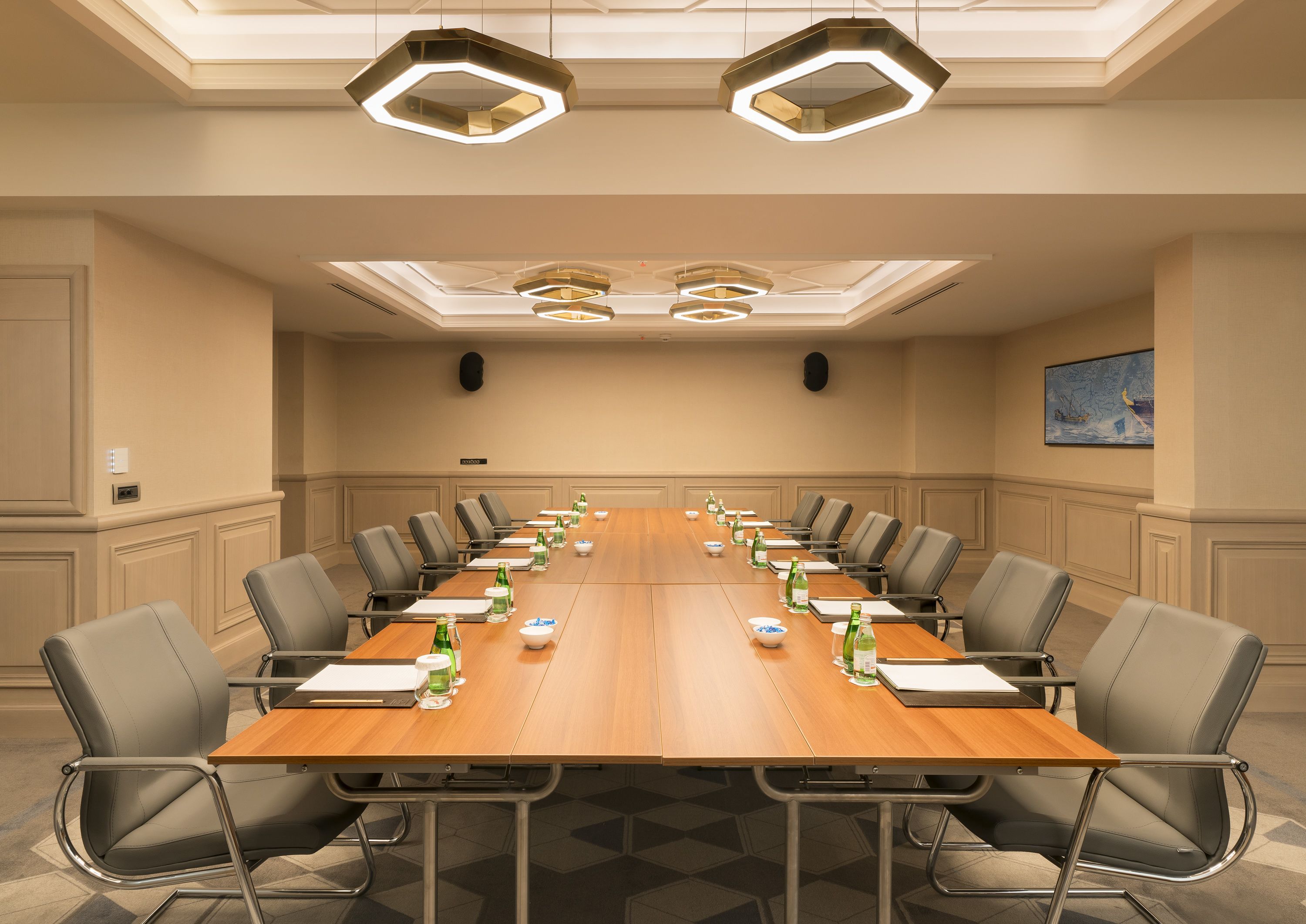 Un salón de conferencias con una larga mesa, varias sillas y lámparas modernas.