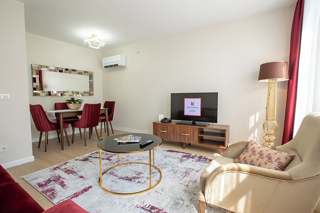 Una sala de estar moderna con una televisión, un comedor con sillas rojas, un sofá y una alfombra estampada.