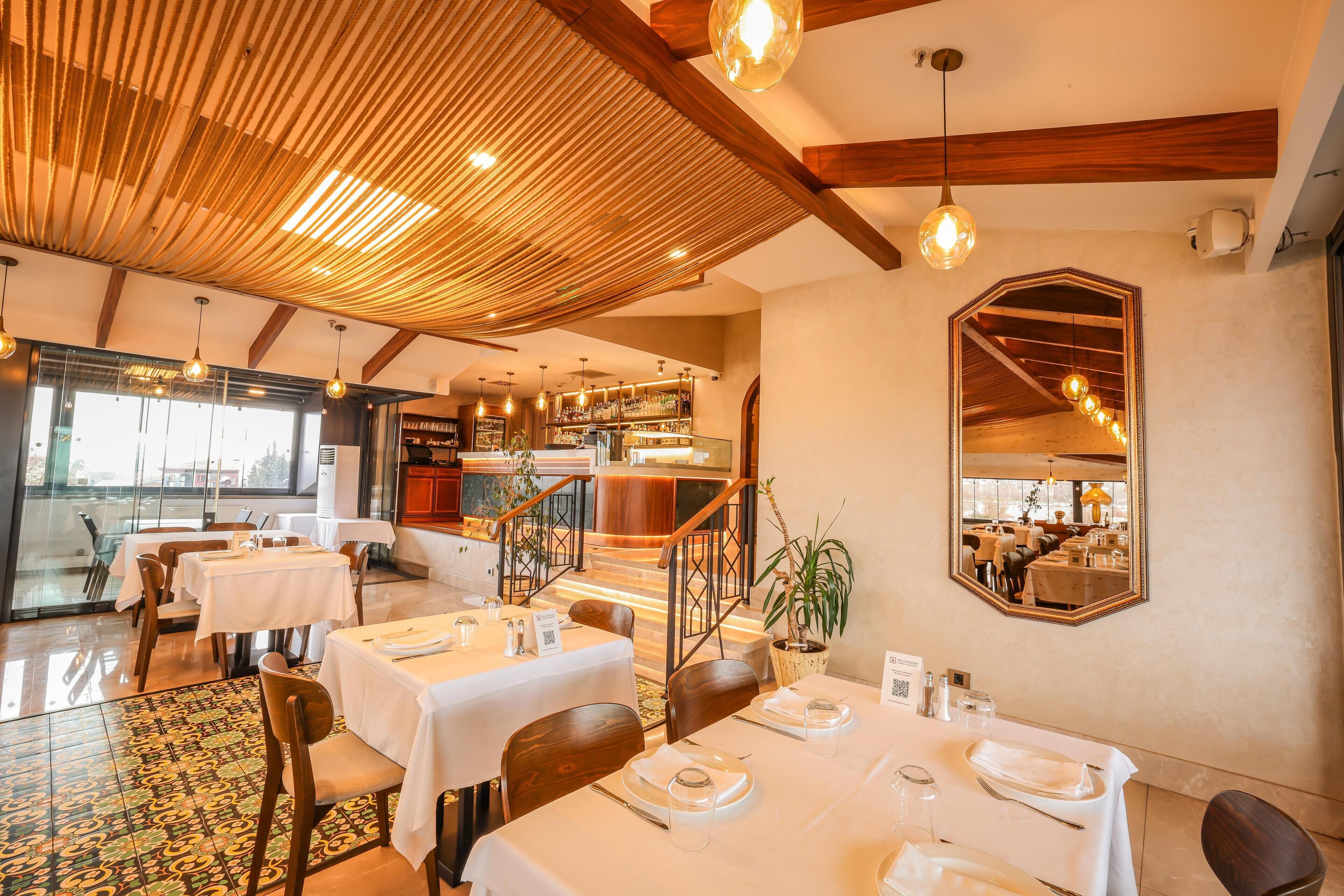 A restaurant with tables set for dining, a staircase leading to an upper level, and a large mirror on the wall.