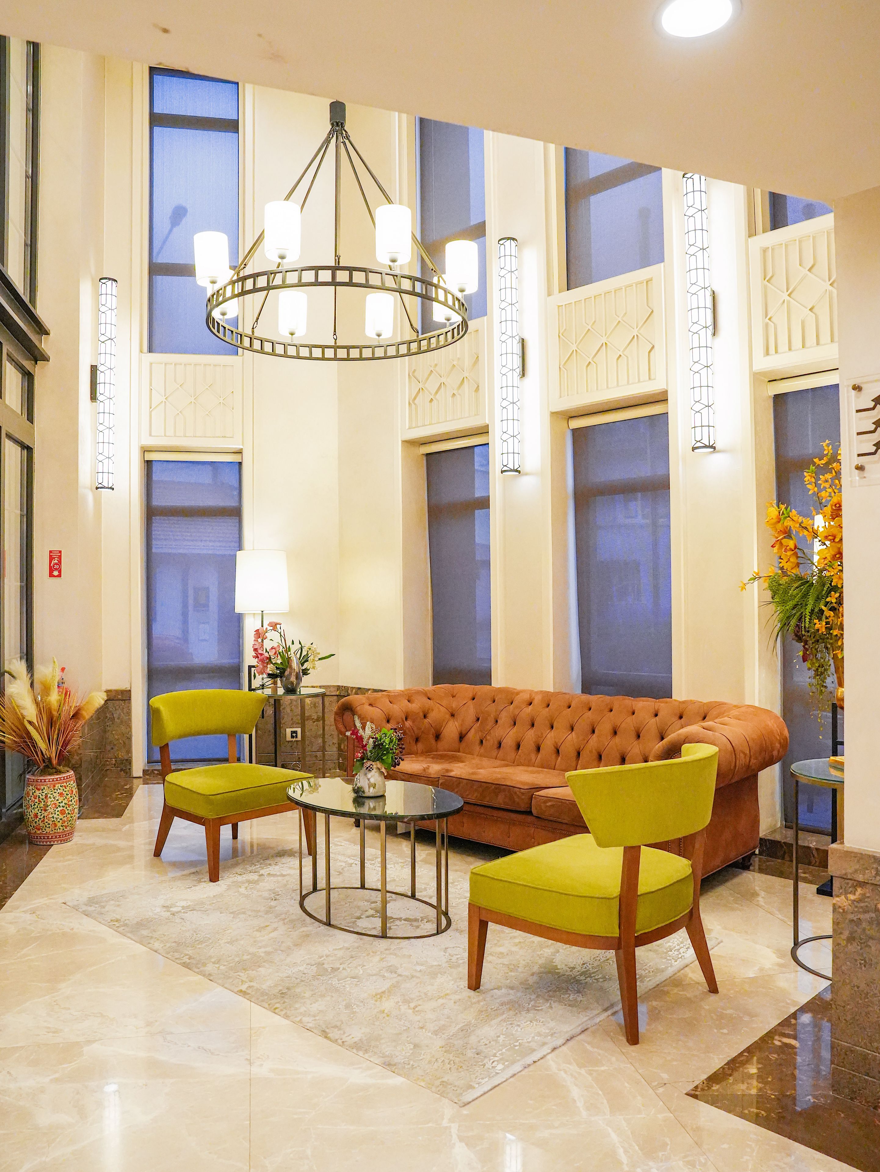 A lobby with a tufted sofa, two armchairs, a glass coffee table, and a chandelier.