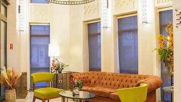 A lobby with a tufted sofa, two armchairs, a glass coffee table, and a chandelier.