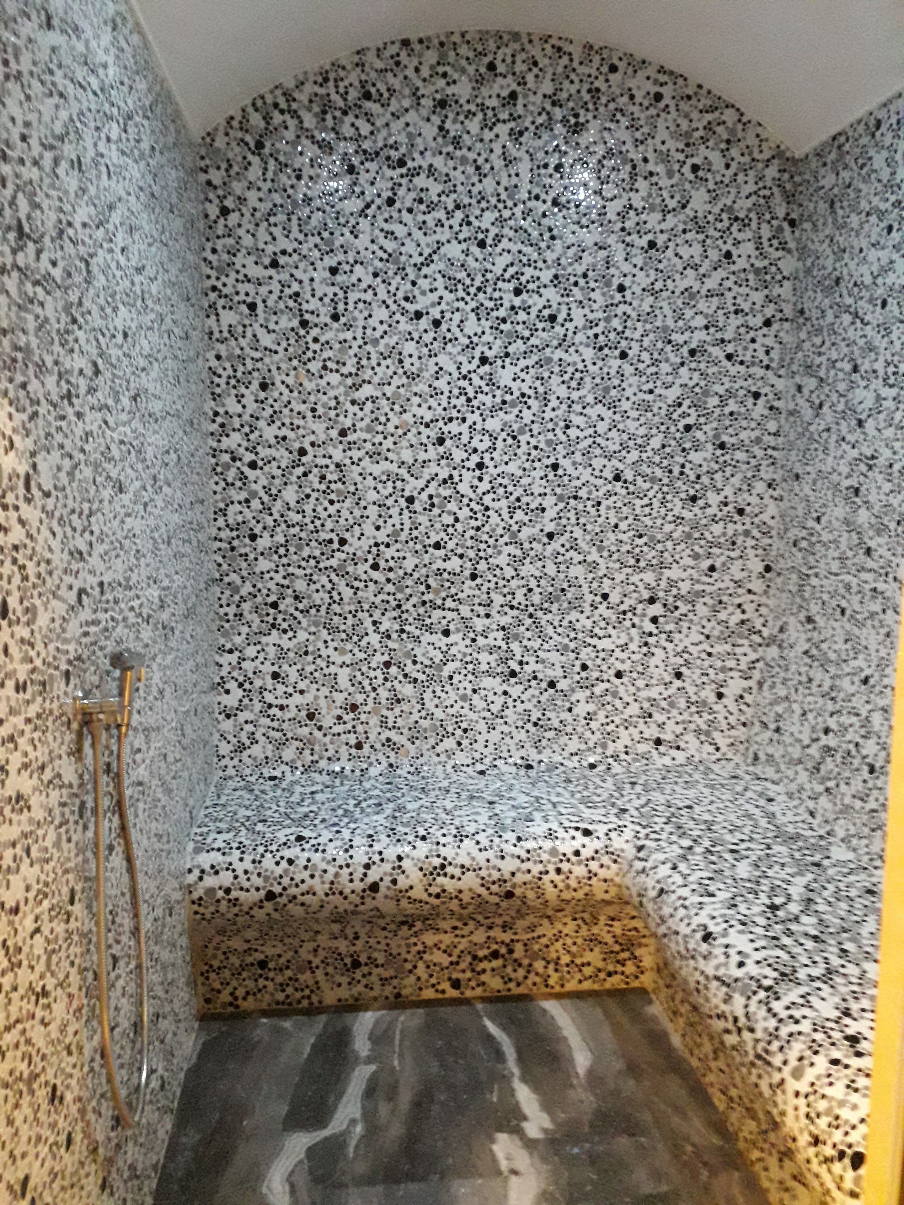Un petit espace douche fermé, avec un mur et un sol recouverts de carreaux à motifs et une pomme de douche dorée.