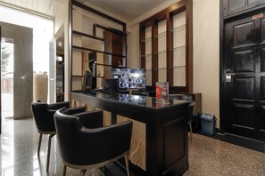 A reception area with a glass counter, black chairs, a television displaying images, and a black door with a number sign. - RedDoorz Plus near Halim Perdanakusuma 2 (Jakarta)