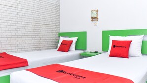 A hotel room with two beds, each with a green headboard, white bedding, and red pillows. There is a small table with a lamp between the beds. - RedDoorz Plus near Hartono Mall (Depok)