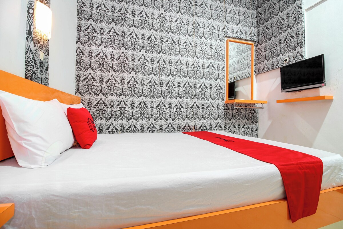 A neatly made bed with white and red bedding, a red throw, and a mirror above it.