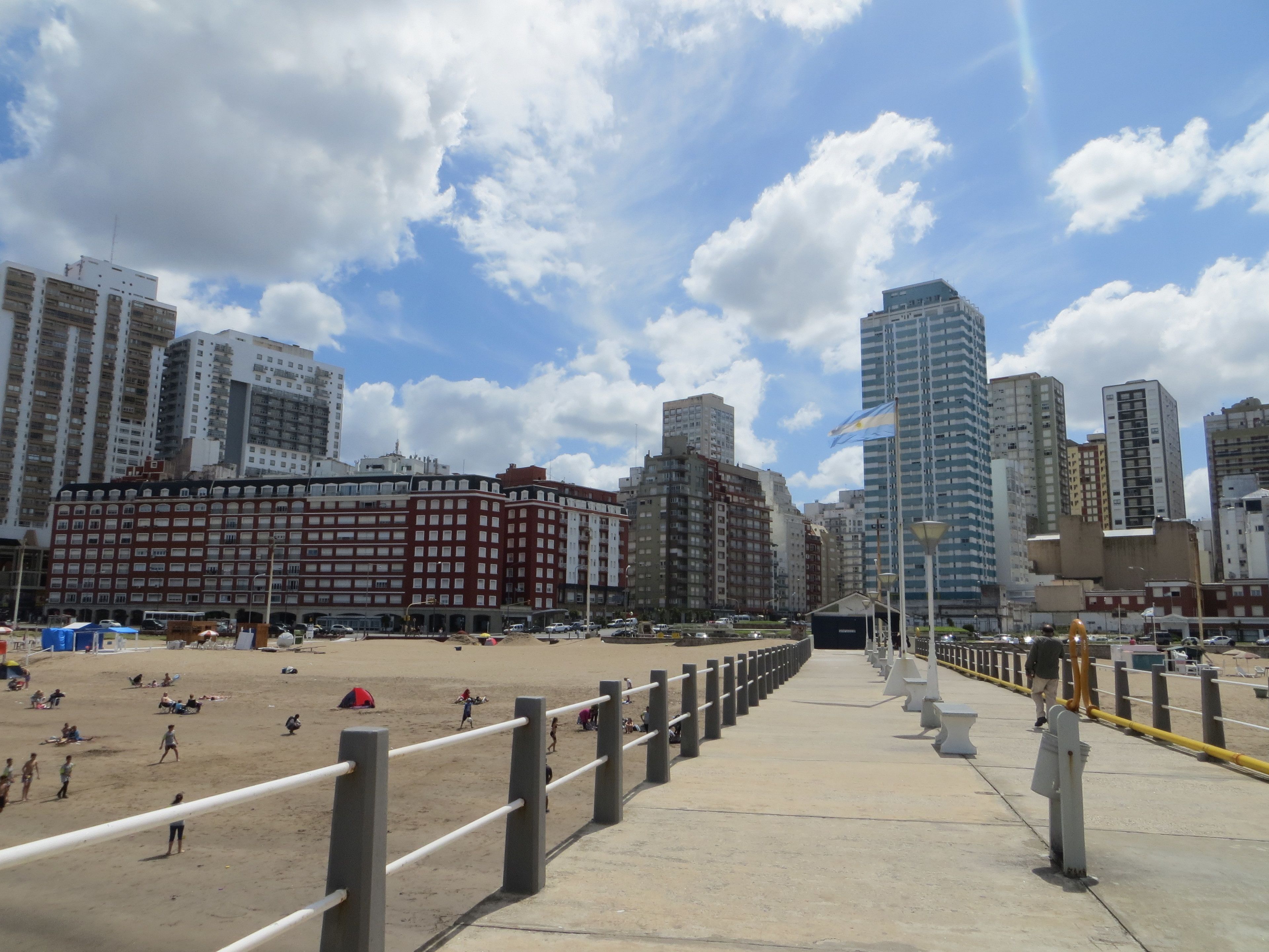 Una playa con un paseo marítimo, edificios altos y cielo despejado.