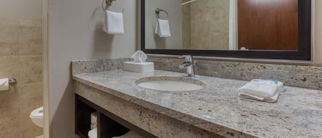 Un baño con encimera de granito, dos lavamanos, un espejo y un perchero para toallas.
