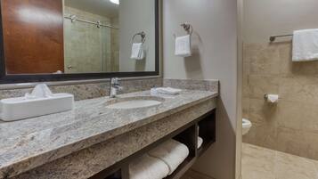 A bathroom with a granite countertop, a sink, a mirror, a towel rack, and a shower area.