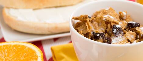 A bowl of cereal with raisins and milk, a half orange, and a sandwich on a plate.