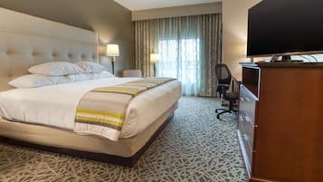 A hotel room with a large bed, two bedside lamps, a television, a desk, and a chair.