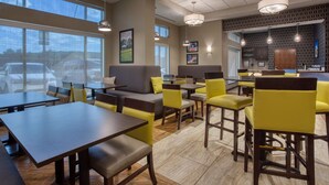 A modern restaurant with high tables, yellow chairs, and a bar area.