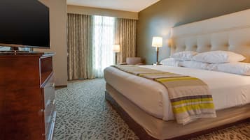 A hotel room with a large bed, a TV, a desk, and a patterned carpet.