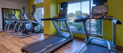 Een sportschool met loopbanden, elliptische trainers en een houten vloer.
