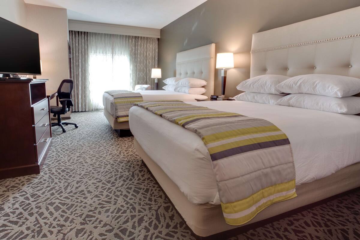 Une chambre d’hôtel avec un grand lit, un lit plus petit, un bureau avec une télévision et une chaise.