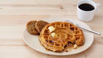 A plate with waffles, syrup, and butter, and a cup of coffee on a wooden table.