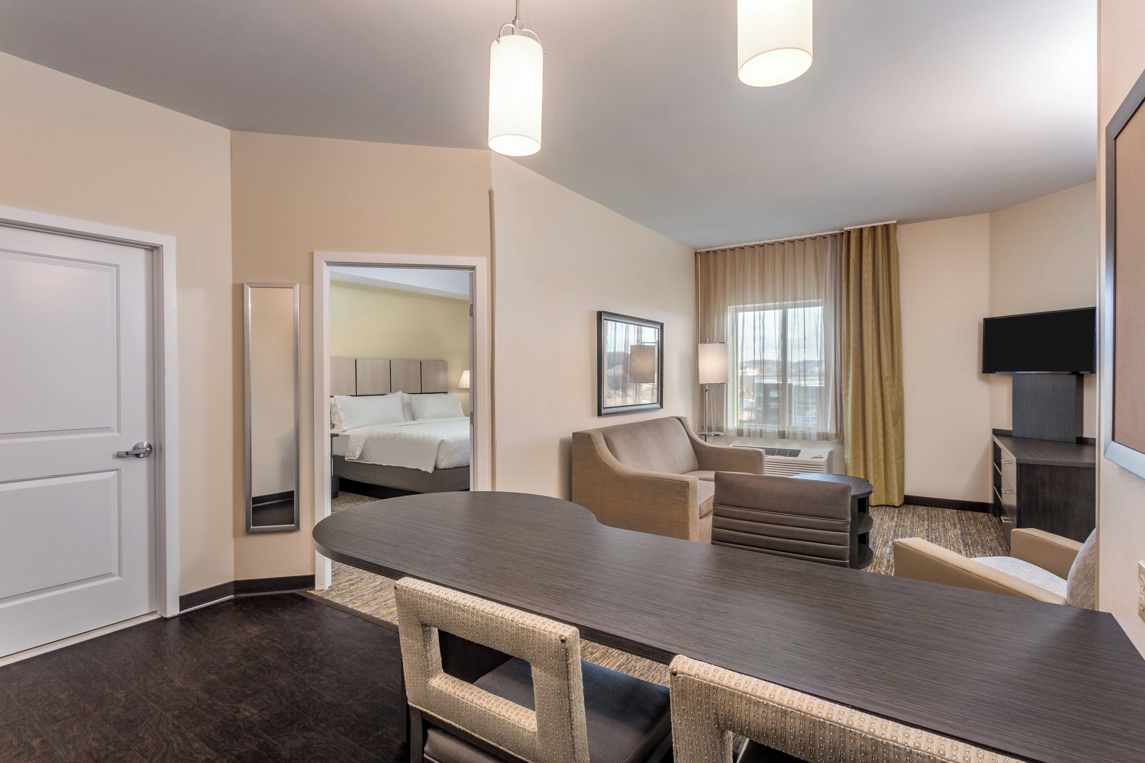 Habitación de hotel con cama, escritorio, silla, televisor y ventana con cortinas.