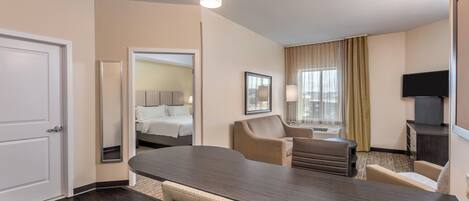Habitación de hotel con cama, escritorio, silla, televisor y ventana con cortinas.