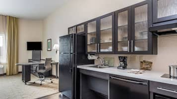 A modern kitchen with dark cabinetry, a built-in refrigerator, a coffee maker, and a small dining area with a desk and chair.