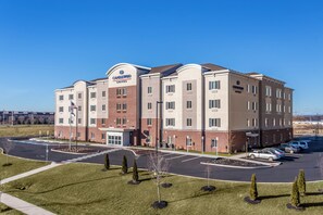 A multi-story hotel with a central entrance, parking lot, and a clear sky.