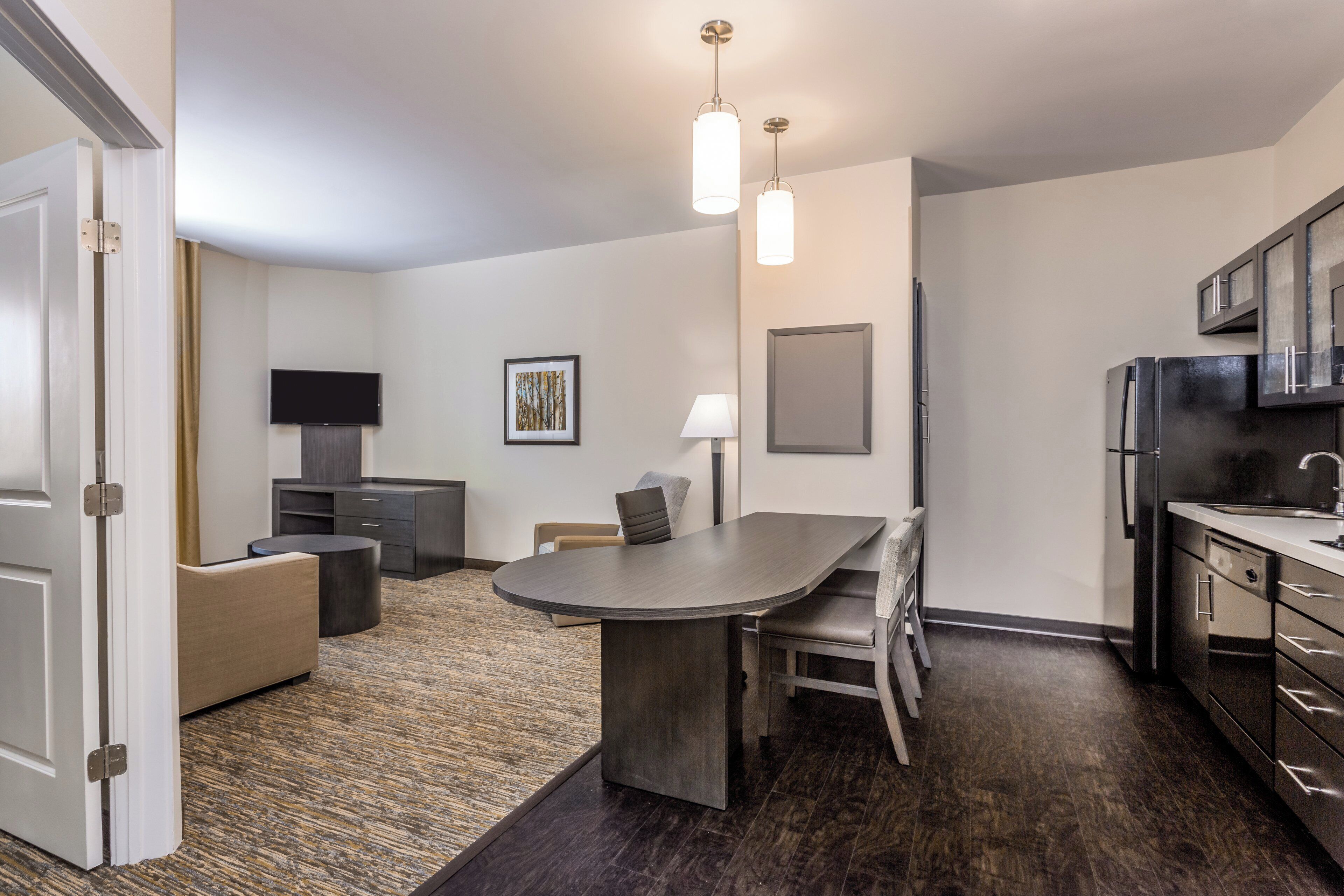 A modern kitchen with dark cabinetry, a built-in refrigerator, and a dining area with a round table and chairs.