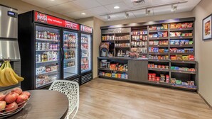 Ein Bereich mit Snacks und Getränken, der Kühlregale, gefüllte Regale und eine Kaffeemaschine umfasst.
