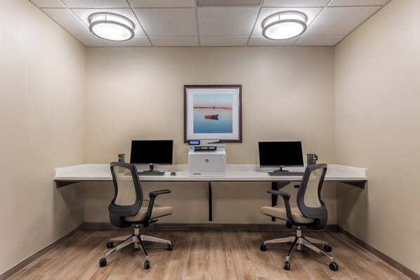 Un salón de conferencias con dos escritorios, cada uno con un monitor de computadora, una impresora y una silla.