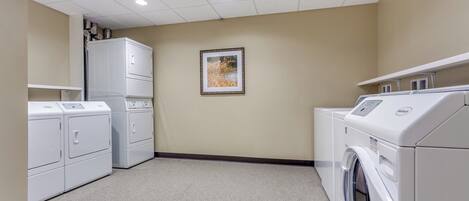 A laundry room with stacked washers and dryers, a ceiling light, and a framed picture on the wall.