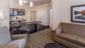Ein modernes Hotelzimmer mit Küchenzeile, Essbereich und Wohnbereich mit Sofa und Couchtisch.