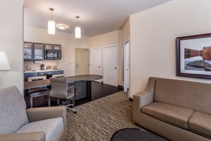 A modern hotel room with a kitchenette, a dining area, and a living space with a sofa and a coffee table.