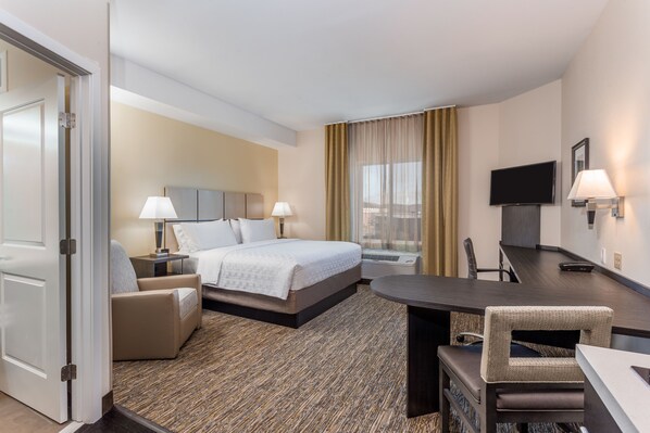 Habitación de hotel con cama, mesitas de noche, escritorio, silla, televisión y ventana con cortinas.