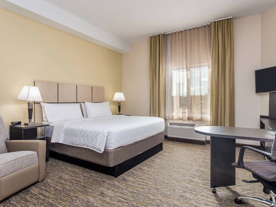 A hotel room with a bed, bedside lamps, a desk, a chair, and a television.