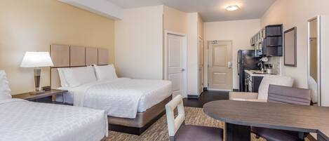 A hotel room with two beds, a dining table, a kitchen area, and a bathroom.