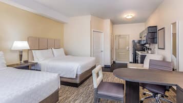 A hotel room with two beds, a desk, a chair, a kitchenette, and a bathroom.