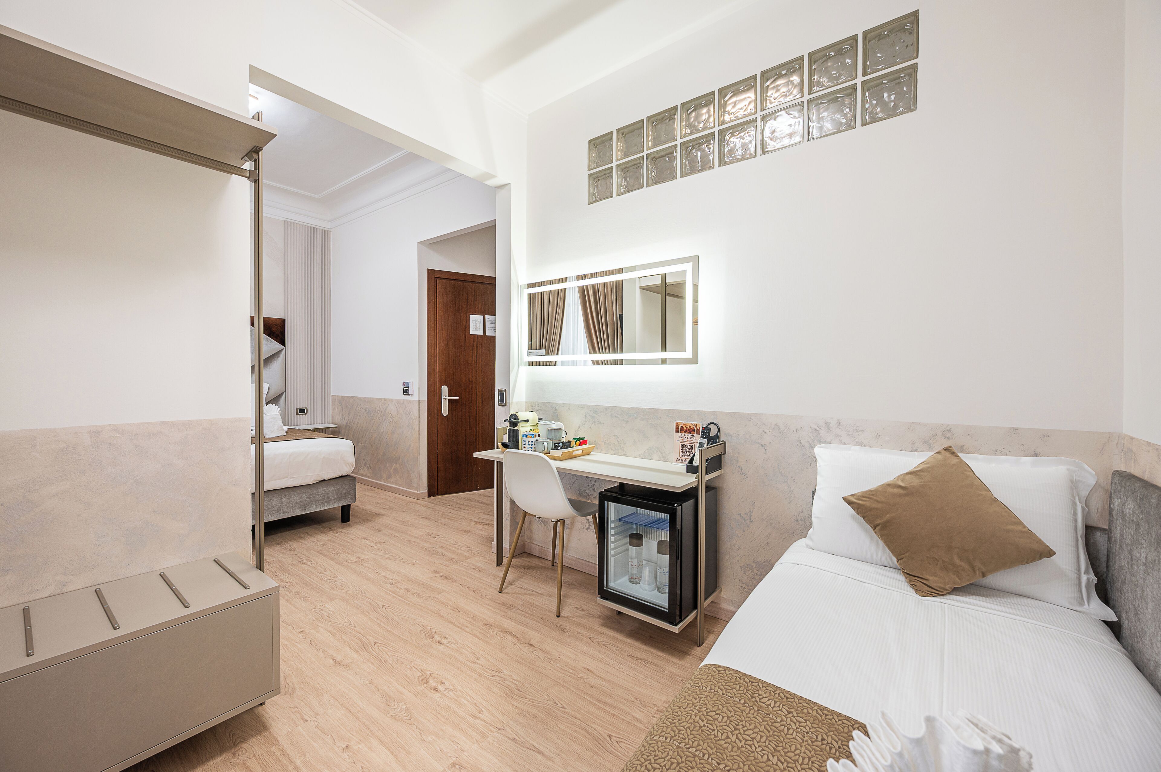 A hotel room with a bed, a desk with a chair, a small refrigerator, and a mirror.