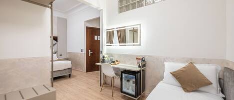 A hotel room with a bed, a desk with a chair, a small refrigerator, and a mirror.
