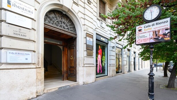 A street view with a building featuring a large arched entrance, signs for 'Cola di Rienz Suite' and 'Luigi Martirani NOTAIO'. - COLA di Rienzo suite (Rome)
