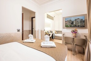 A hotel room with a bed, a desk, a chair, a painting, and a bathroom visible through an open door.