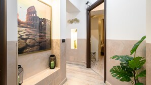 A hallway with a framed picture of the Colosseum, a small statue, and a potted plant. - COLA di Rienzo suite (Rome)