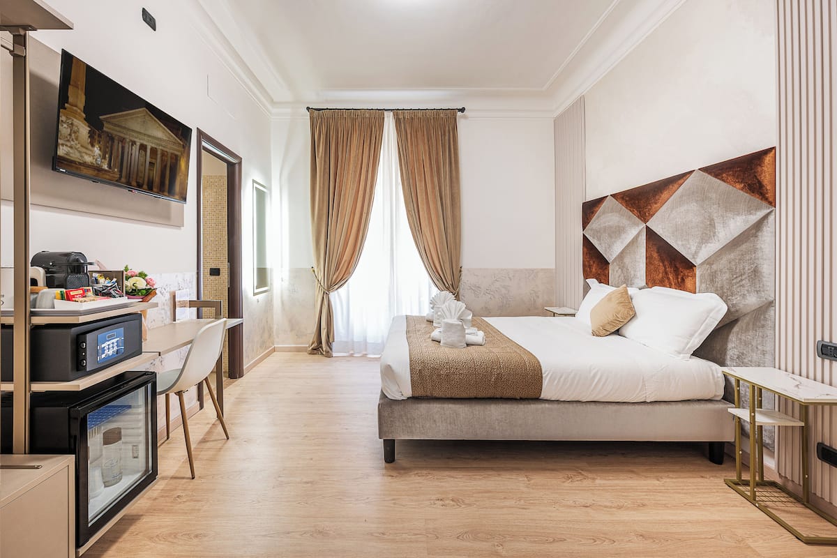 Una habitación de hotel moderna con cama, escritorio, computadora, televisión y minibar.
