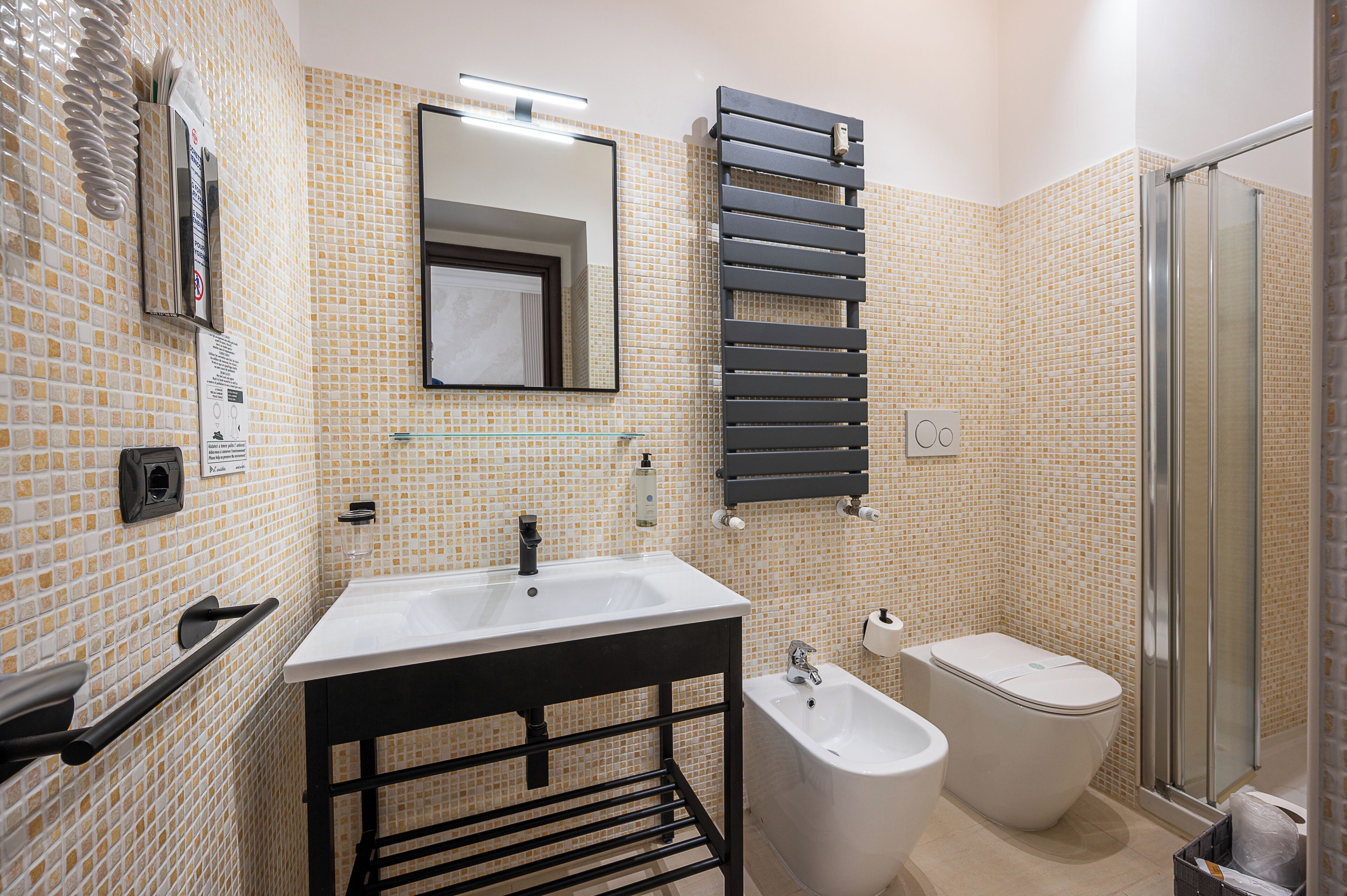 A bathroom with a sink, mirror, towel rack, bidet, and shower.