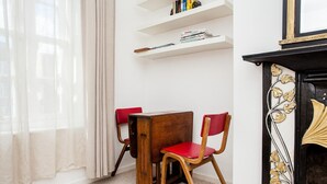 A room with a wooden table and two red chairs, a white shelf with books, and a decorative fireplace. - Stylish One Bedroom Flat in Vauxhall (London)