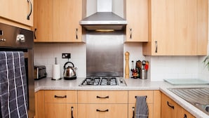 A modern kitchen with wooden cabinets, a stainless steel range hood, a gas stove, and a kettle. - Stylish One Bedroom Flat in Vauxhall (London)