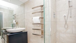 Et moderne badeværelse med et glasbadeværelsesafskærmning, et sort møbel med en hvid vask og kromhåndklædetørrestativer.