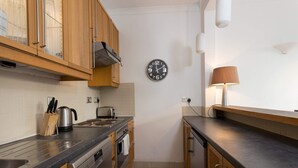 Uma cozinha compacta com armários de madeira, uma pia de aço inoxidável, uma chaleira e um relógio na parede.