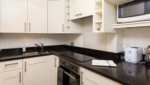 A modern kitchen with white cabinets, a black countertop, a built-in microwave, a toaster, and a sink. - 1 Bedroom Flat in South Kensington (London)